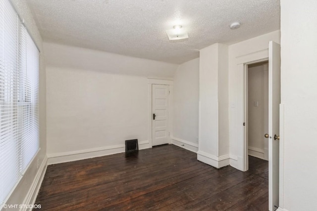 spare room featuring lofted ceiling, dark wood-type flooring, and a textured ceiling