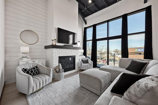 living room with wood walls, a brick fireplace, a towering ceiling, and light hardwood / wood-style flooring