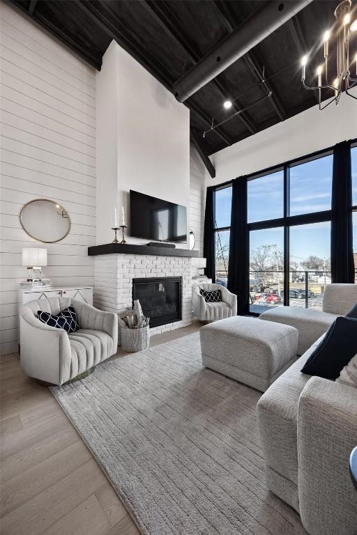 living area with a fireplace, a towering ceiling, wooden walls, wood finished floors, and beamed ceiling