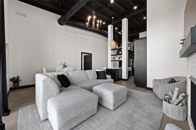 living room featuring a towering ceiling, hardwood / wood-style floors, a stone fireplace, and an inviting chandelier