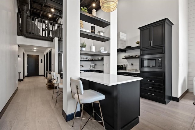 kitchen with dark cabinets, light countertops, built in microwave, open shelves, and a kitchen bar