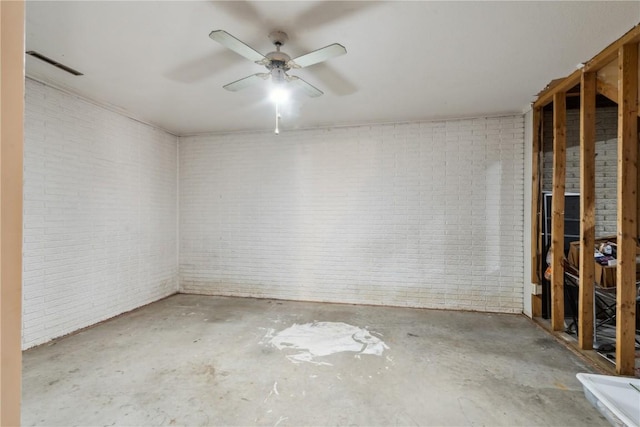 spare room featuring ceiling fan, brick wall, and concrete flooring