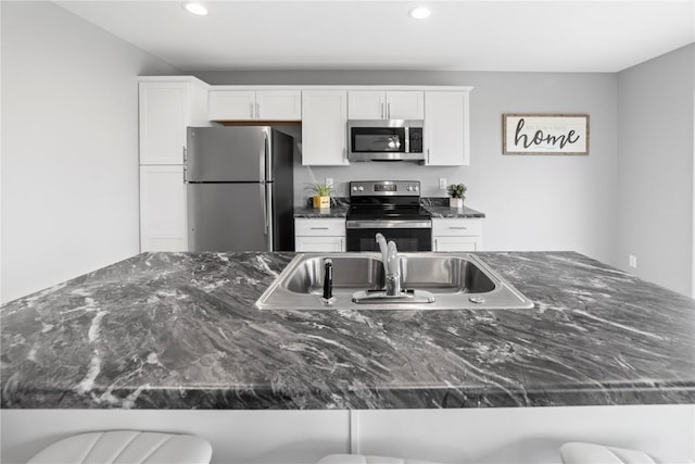 kitchen with appliances with stainless steel finishes, a kitchen bar, white cabinetry, and sink