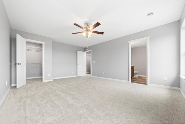 unfurnished bedroom with ceiling fan, light colored carpet, connected bathroom, a walk in closet, and a closet