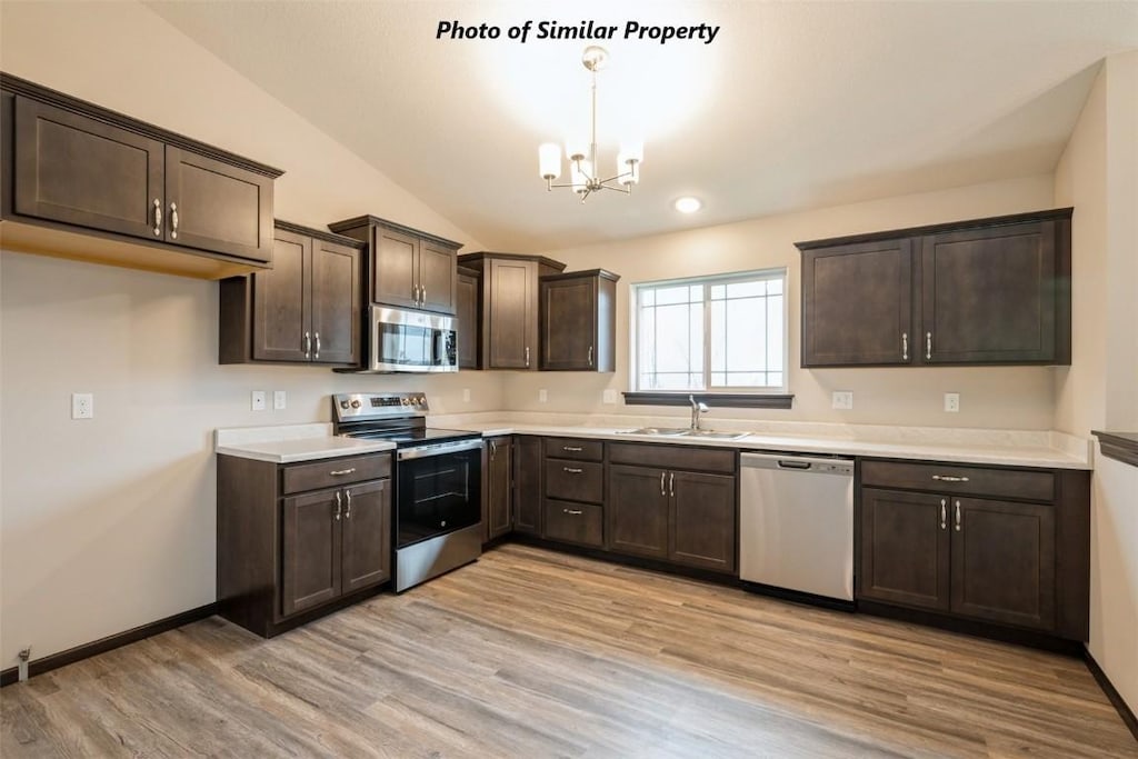 kitchen with stainless steel appliances, hanging light fixtures, vaulted ceiling, light hardwood / wood-style flooring, and sink