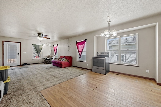 living room featuring ceiling fan with notable chandelier, light hardwood / wood-style flooring, and a textured ceiling