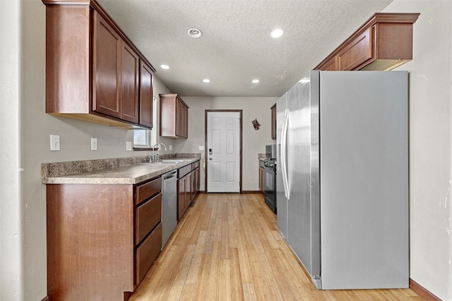 kitchen with stainless steel appliances, sink, a textured ceiling, and light hardwood / wood-style flooring