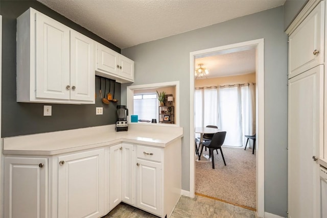 kitchen with light carpet, white cabinetry, and a textured ceiling