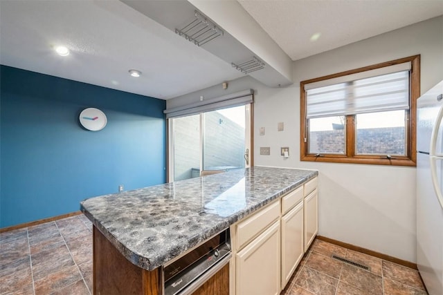 kitchen with cream cabinetry, kitchen peninsula, light stone counters, and white refrigerator