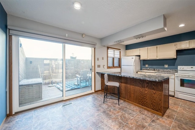 kitchen featuring a breakfast bar, white appliances, sink, and dark stone countertops