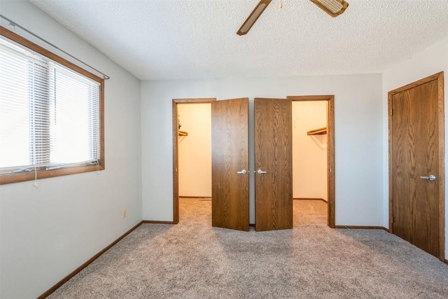 unfurnished bedroom featuring ceiling fan, light colored carpet, a spacious closet, a textured ceiling, and a closet