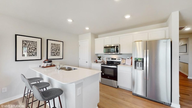 kitchen with light hardwood / wood-style floors, a breakfast bar, sink, white cabinetry, and appliances with stainless steel finishes