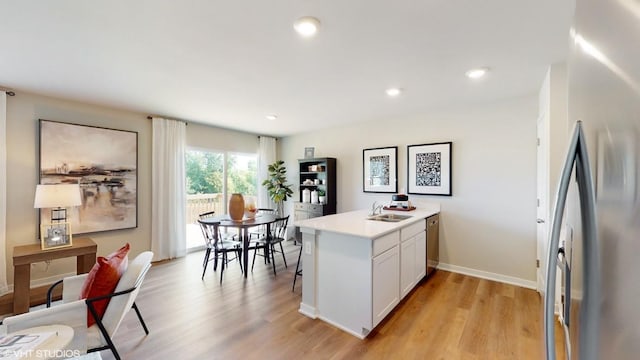 kitchen featuring white cabinetry, kitchen peninsula, light wood-type flooring, stainless steel refrigerator, and sink