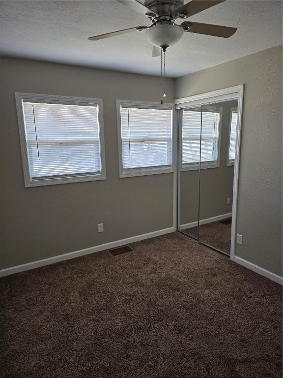 unfurnished bedroom with ceiling fan, a closet, and dark colored carpet