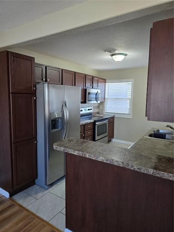 kitchen with kitchen peninsula, sink, appliances with stainless steel finishes, a textured ceiling, and light tile patterned floors