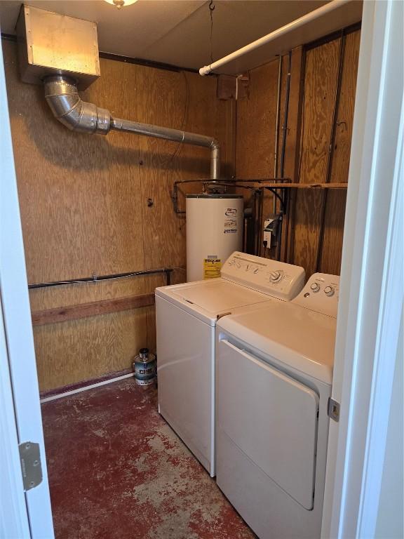 laundry area featuring water heater, wood walls, and washing machine and clothes dryer