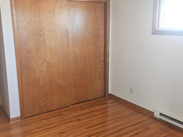 unfurnished bedroom featuring wood-type flooring, a baseboard heating unit, and a closet