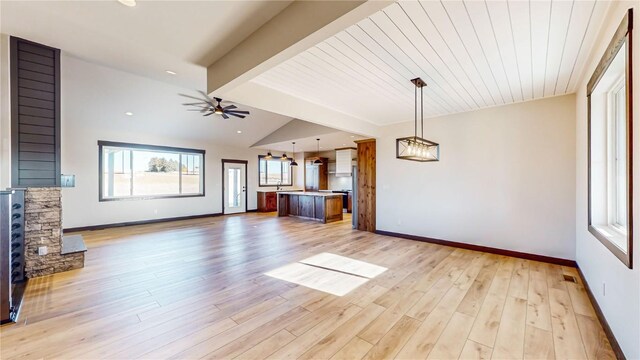 unfurnished living room featuring ceiling fan, lofted ceiling with beams, light wood-type flooring, wood ceiling, and a stone fireplace