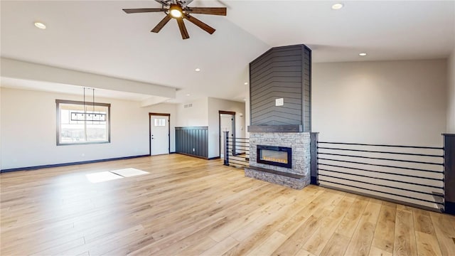 unfurnished living room with vaulted ceiling, a stone fireplace, baseboards, light wood-style floors, and ceiling fan