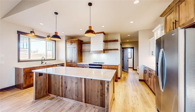 kitchen featuring decorative light fixtures, a kitchen island, sink, light wood-type flooring, and appliances with stainless steel finishes