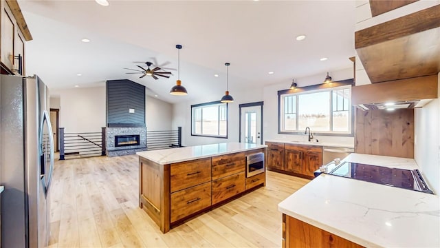 kitchen with stainless steel appliances, a kitchen island, a sink, light wood finished floors, and brown cabinets