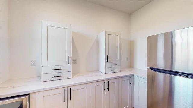 kitchen featuring light stone countertops, beverage cooler, white cabinets, and stainless steel refrigerator