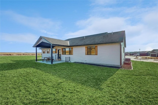 back of house featuring roof with shingles, a patio area, and a lawn