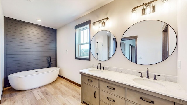 full bath featuring double vanity, a sink, a soaking tub, and wood finished floors