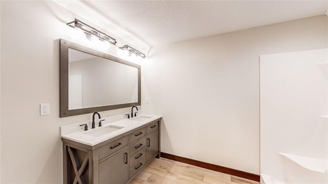 full bath with double vanity, a sink, baseboards, and wood finished floors