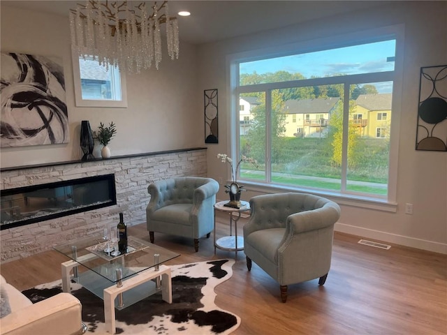 sitting room with a healthy amount of sunlight, a fireplace, a chandelier, and light hardwood / wood-style flooring