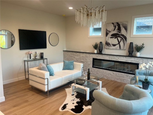 living room with light wood-type flooring, an inviting chandelier, and a stone fireplace