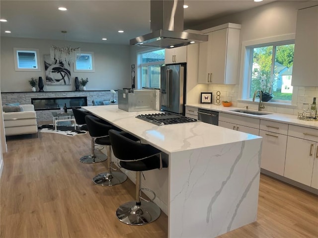 kitchen with light stone countertops, white cabinets, a kitchen island, stainless steel appliances, and island range hood