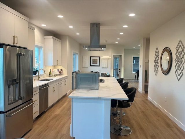 kitchen with a kitchen bar, sink, island exhaust hood, white cabinetry, and stainless steel appliances