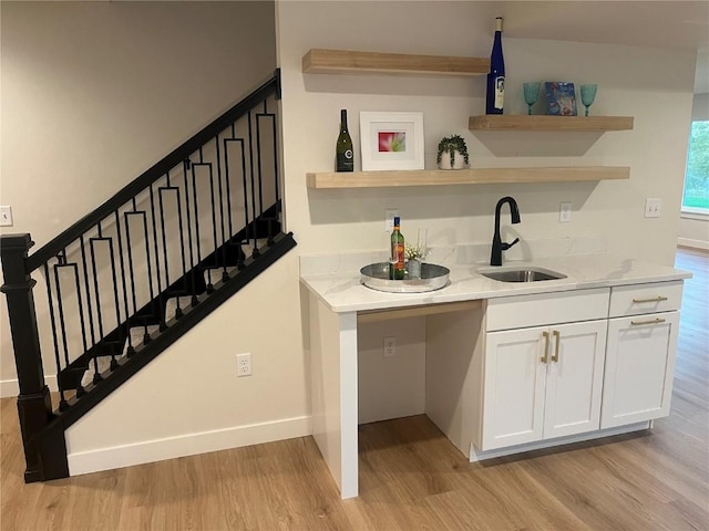 bar with white cabinets, sink, light stone counters, and light hardwood / wood-style flooring