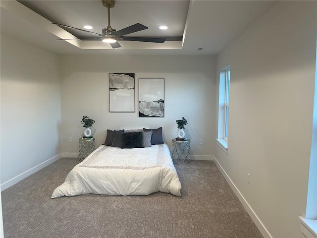 bedroom featuring ceiling fan, multiple windows, a raised ceiling, and carpet flooring