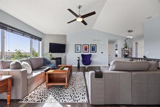 living room featuring vaulted ceiling, ceiling fan, a tiled fireplace, and dark hardwood / wood-style floors