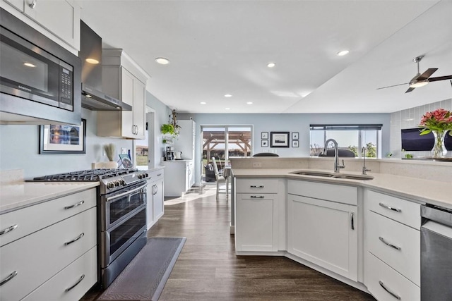 kitchen with wall chimney range hood, white cabinetry, appliances with stainless steel finishes, and sink