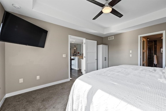 carpeted bedroom featuring ceiling fan, connected bathroom, and a tray ceiling