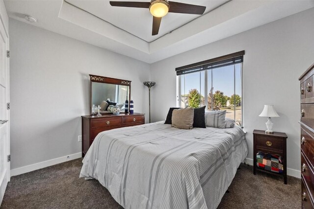 bedroom with ceiling fan, dark carpet, and a tray ceiling