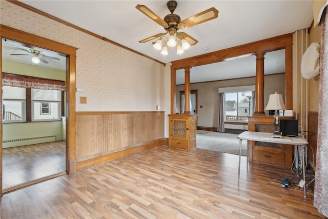 empty room featuring crown molding, ceiling fan, a baseboard heating unit, decorative columns, and light wood-type flooring