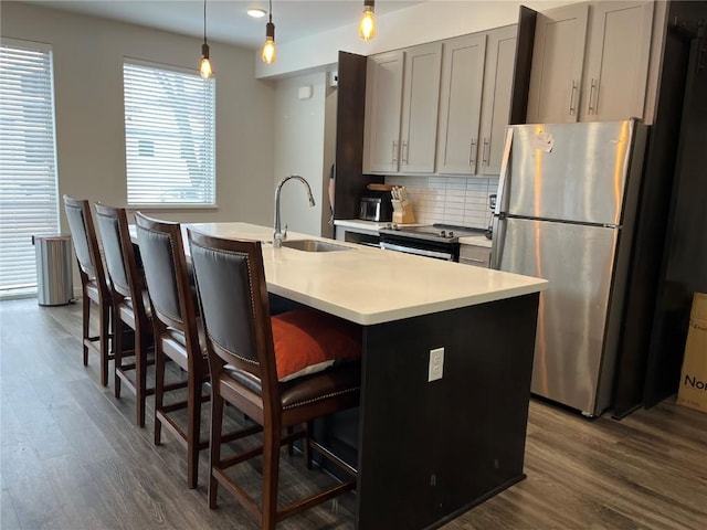 kitchen with stainless steel appliances, sink, hanging light fixtures, gray cabinets, and a center island with sink