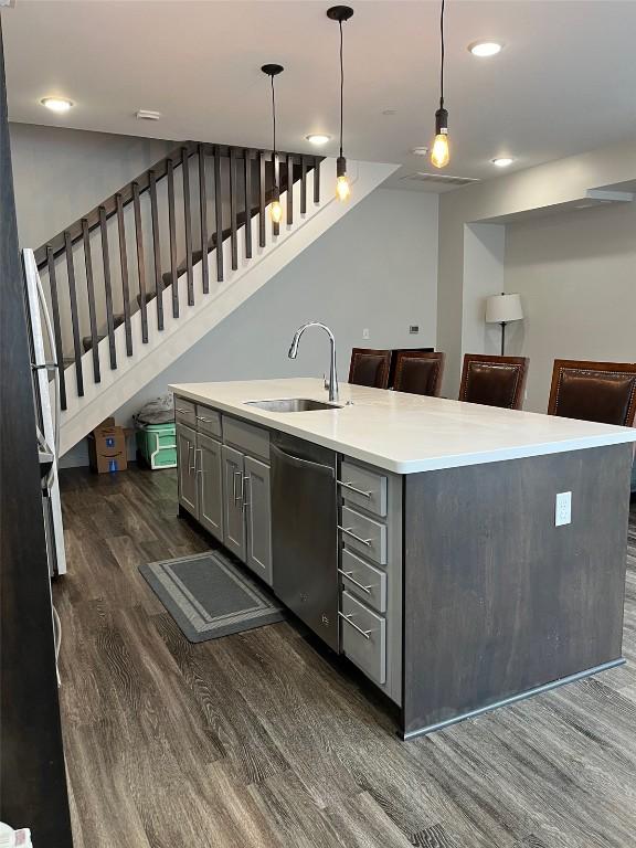 kitchen with a kitchen island with sink, stainless steel dishwasher, sink, decorative light fixtures, and gray cabinets