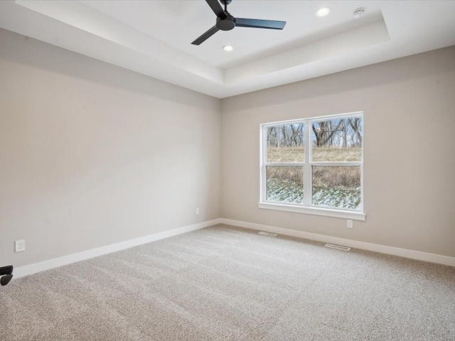 carpeted empty room featuring a raised ceiling and ceiling fan