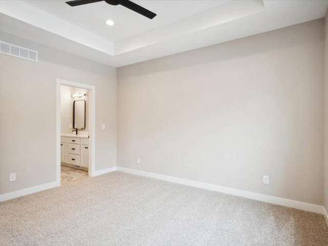 unfurnished bedroom with connected bathroom, sink, light carpet, a tray ceiling, and ceiling fan