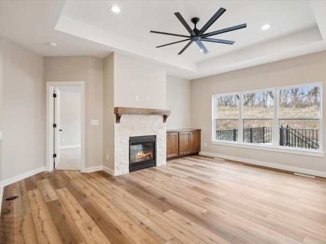 unfurnished living room with a raised ceiling, ceiling fan, a fireplace, and light hardwood / wood-style flooring