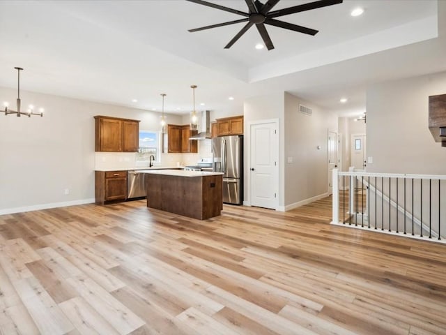 kitchen featuring pendant lighting, a kitchen island, wall chimney exhaust hood, and appliances with stainless steel finishes