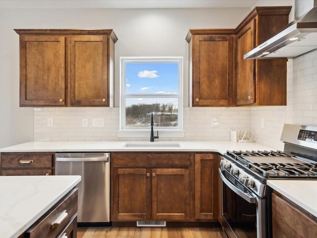 kitchen featuring appliances with stainless steel finishes, sink, wall chimney range hood, and decorative backsplash