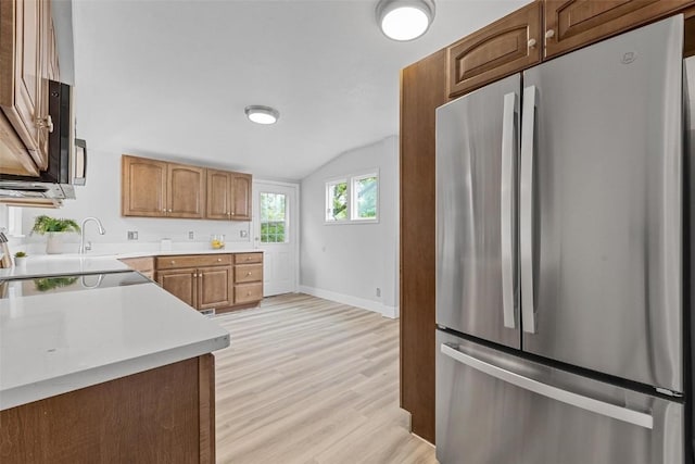 kitchen featuring black electric stovetop, stainless steel fridge, light hardwood / wood-style floors, and vaulted ceiling