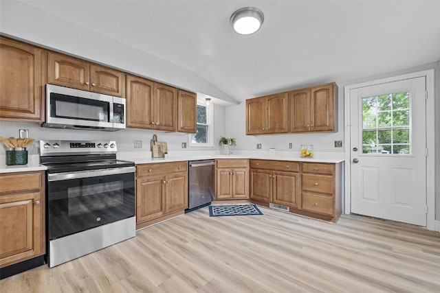 kitchen with vaulted ceiling, appliances with stainless steel finishes, plenty of natural light, and light hardwood / wood-style flooring