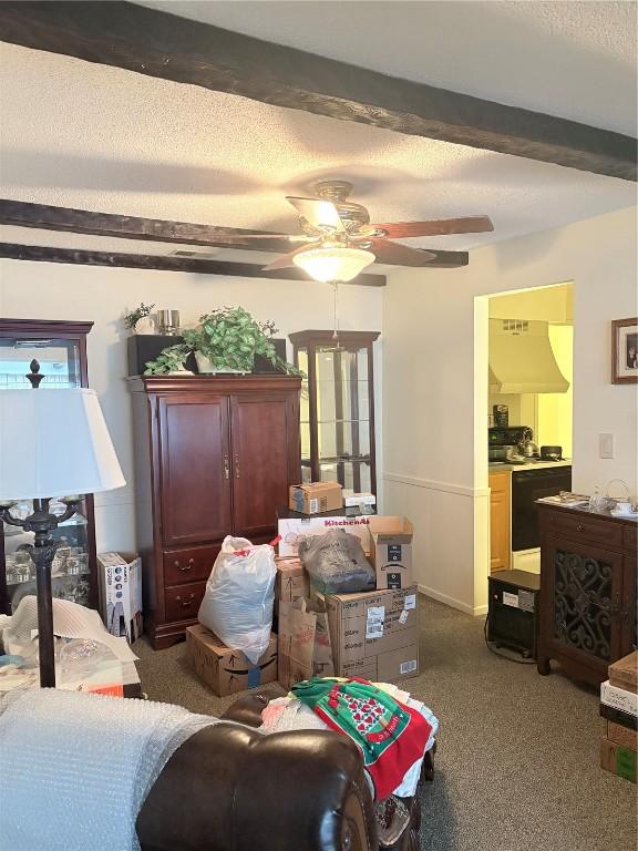 living room featuring beamed ceiling, ceiling fan, carpet floors, and a textured ceiling